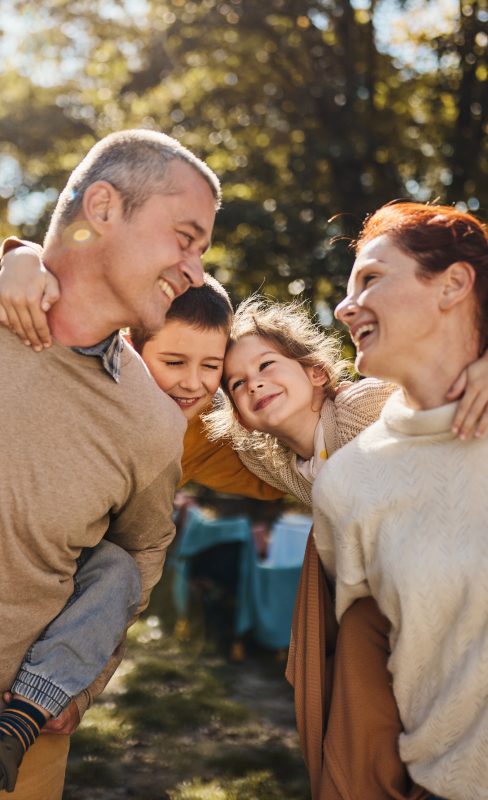 Happy parents having fun while piggybacking their small kids during autumn day in nature.